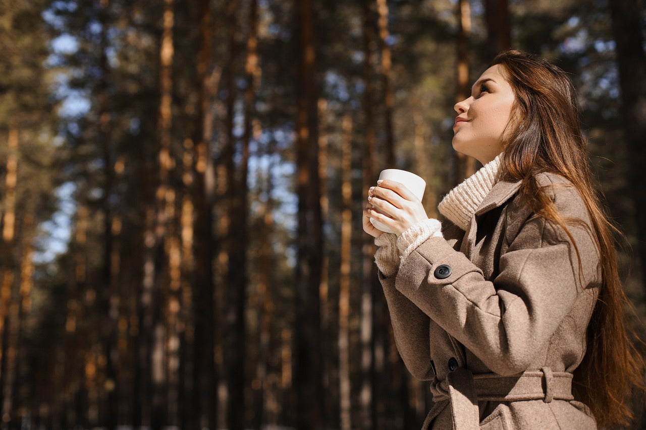 An image of a young woman in a forest enjoying coffee